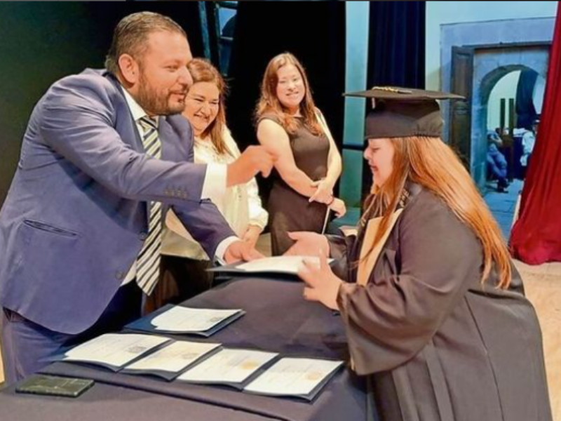 A young graduate shakes a man's hand while receiving her certificate
