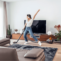 A young happy woman listen to music and cleaning her living room