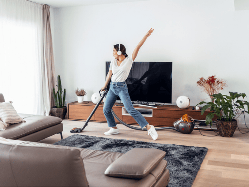 A young happy woman listen to music and cleaning her living room