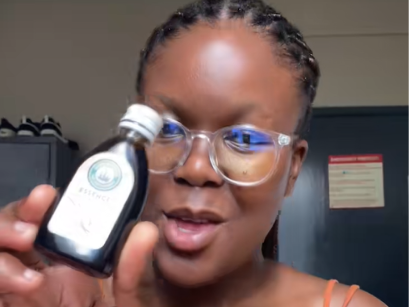 A young lady with spectacles holding up a bottle of vanilla essence
