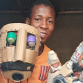 A young man holding up his robotics project made from basic materials
