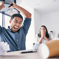 A young man sitting at his desk gets frustrated and is about to throw his tablet