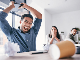 A young man sitting at his desk gets frustrated and is about to throw his tablet