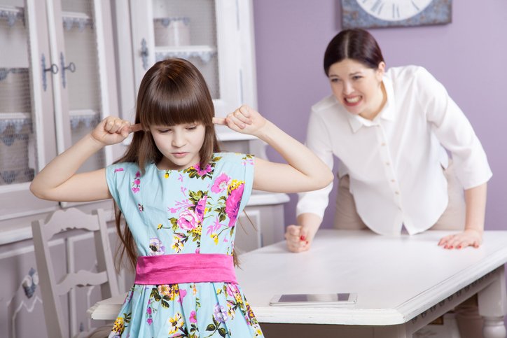 Adult shouting while young girl has her ears blocked