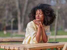African woman enjoying a moment at a park while sitting at a wooden table in bright daylight