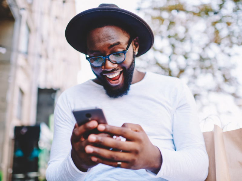 An African guy wearing a hat is excited as he looks at his phone