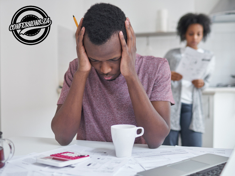 An African male sitting at kitchen table with calculator and woman holding bill in the background