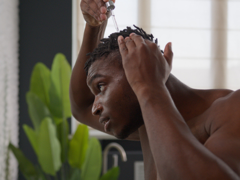 An African man applies oil to his hair using a dropper