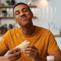An African man holding a sandwich and enjoying a bite with his eyes closed