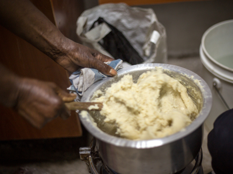 An African woman prepares pap in an aluminum pot using a wooden spoon