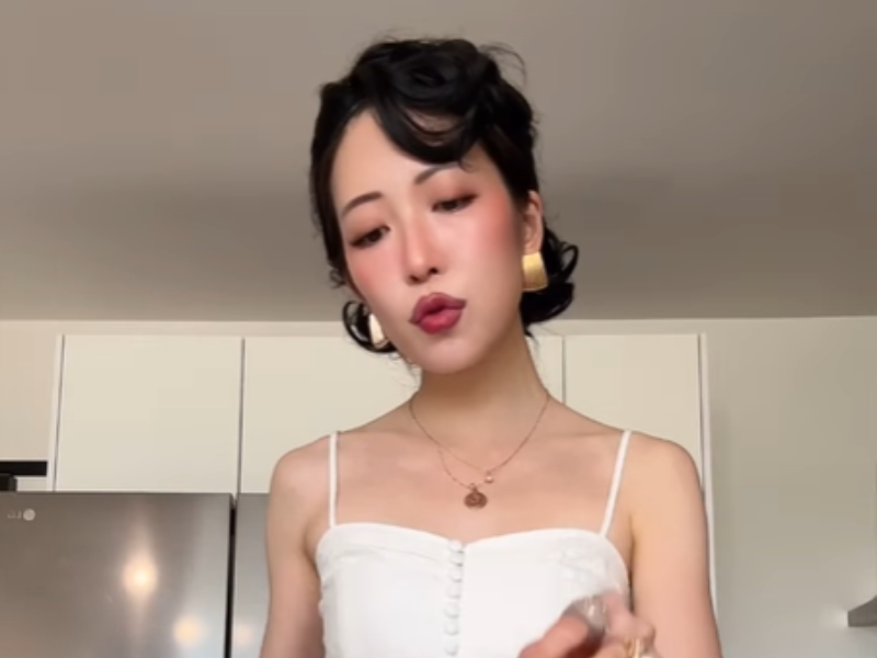 An Asian woman wearing a white dress preparing something in the kitchen