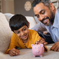 An Indian boy puts money into his piggy bank with his father