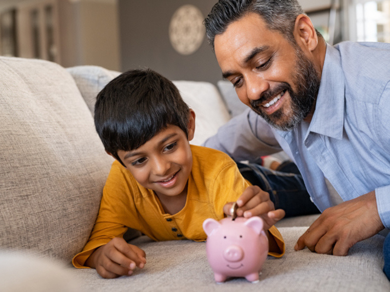 An Indian boy puts money into his piggy bank with his father