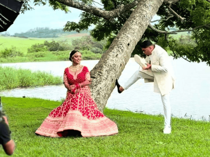 An Indian bride sits on a tree while the groom dusts his shoe