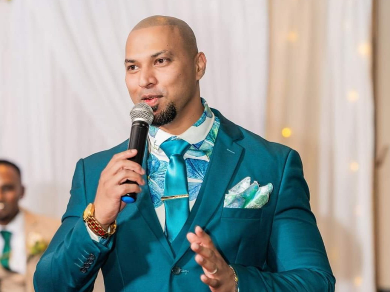 An Indian man dressed in turquoise suit speaking with a microphone