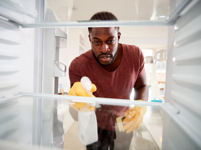 An adult man cleaning inside a refridgerator