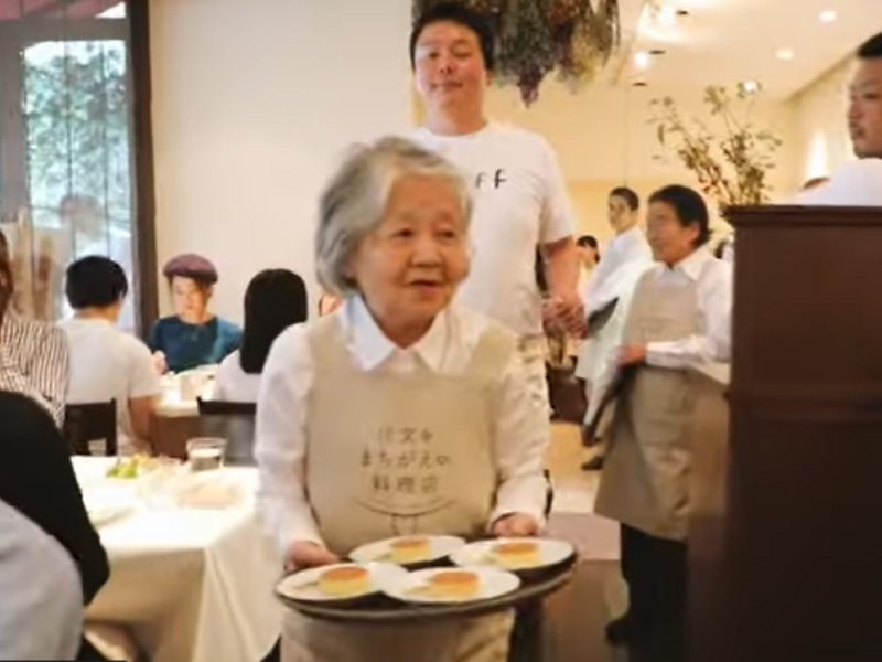 An elderly female waitress carrying tray of food