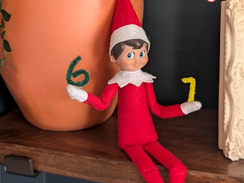 An elf on the shelf holding the numbers six and seven