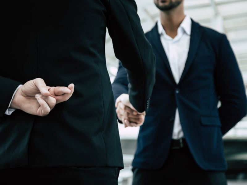 An employee crossing his fingers at his back and shakes hands with manager