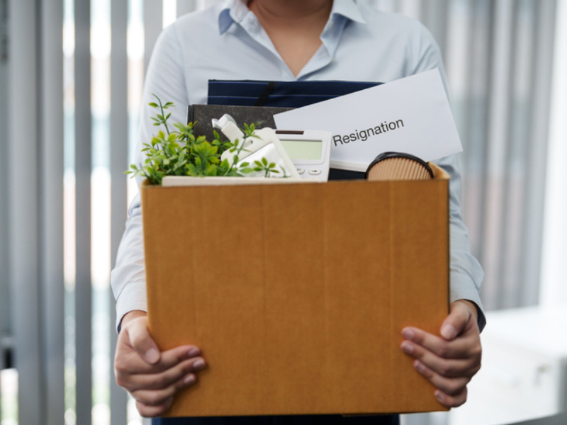 An employee holds a box with their belongings and a resignation letter