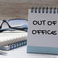 An out of office notice written on a notepad displayed on a desk