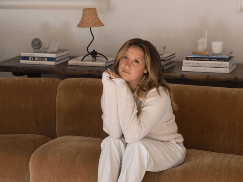 Ashley Tisdale sitting on a plush, curved brown sofa
