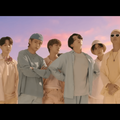 BTS members pose against a blue and pink sky backdrop