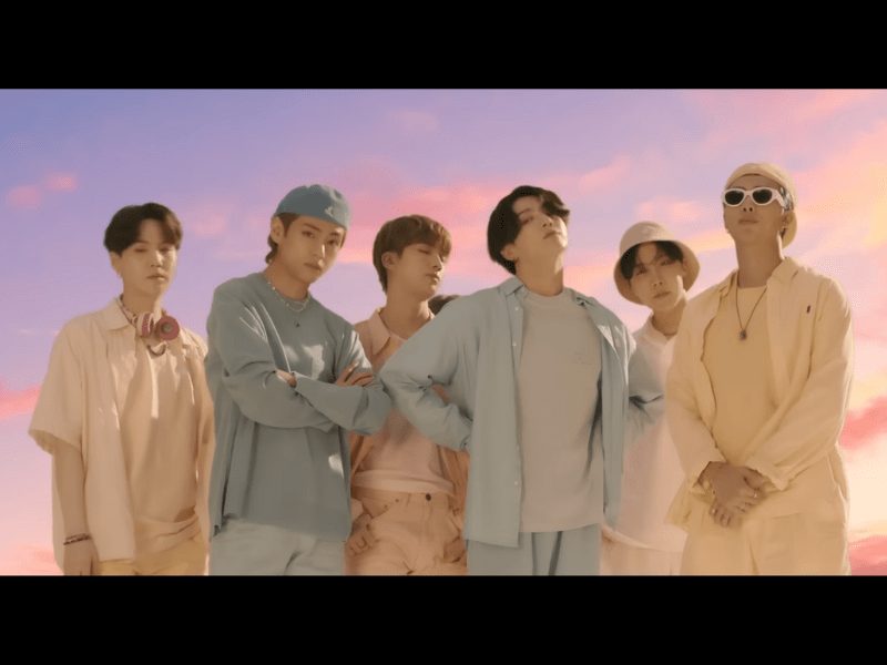 BTS members pose against a blue and pink sky backdrop