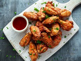 Baked chicken wings with sesame seeds and sweet chili sauce on white wooden board