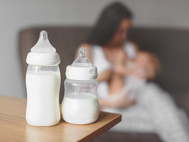 Bottles with breast milk on the background of mother holding in her hands and breastfeeding baby