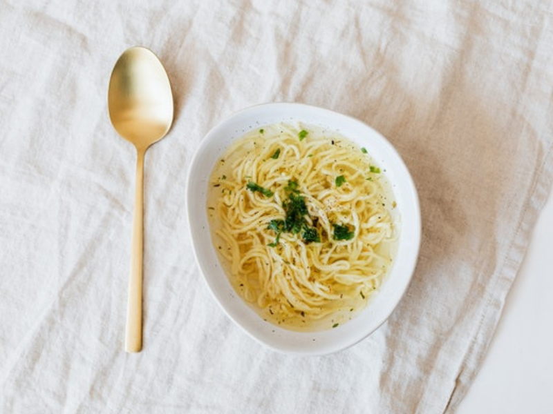 Bowl of noodles with gold plated spoon on table