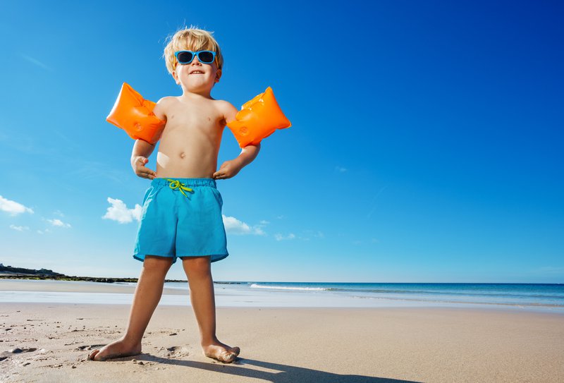 Boy in inflatable shoulder straps stand on the ocean beach