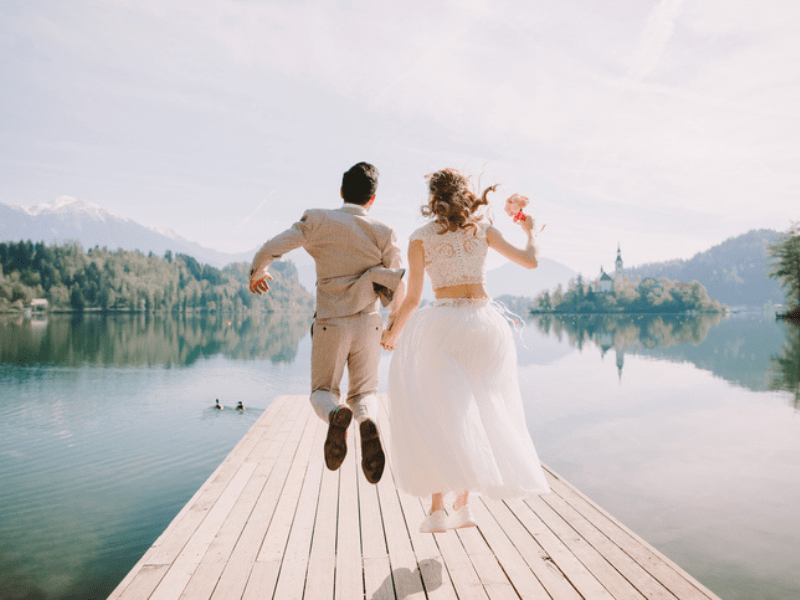 Bride and groom jump for joy on a wooden pier