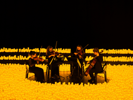 Four string players perform while surrounded by thousands of candles