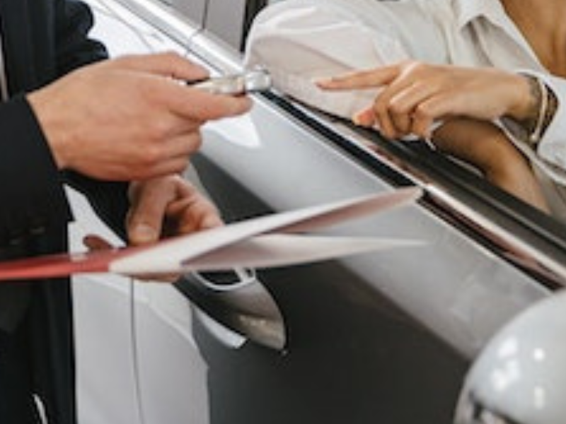 Car dealer handing in keys to a woman sitting in new car