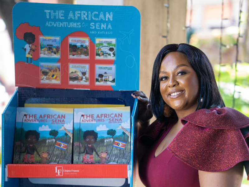 Carol Ofori posing next to her book series, The African Adventures of Sena and Katlego