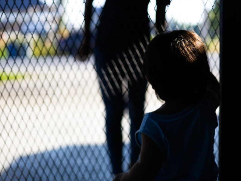 Child is standing behind a fence and a stranger's silhouette is seen