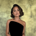 Chrissy Teigen  poses against a green-gold studio backdrop