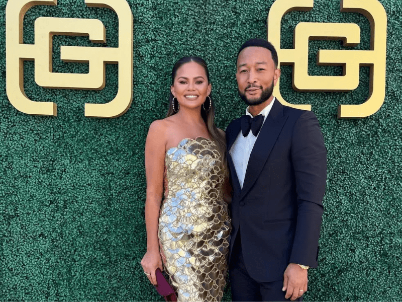 Chrissy Teigen and John Legend pose in front of a green backdrop