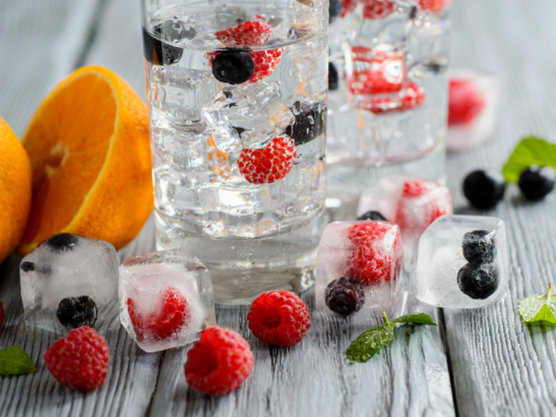 Cold cocktail with berries frozen in ice cubes