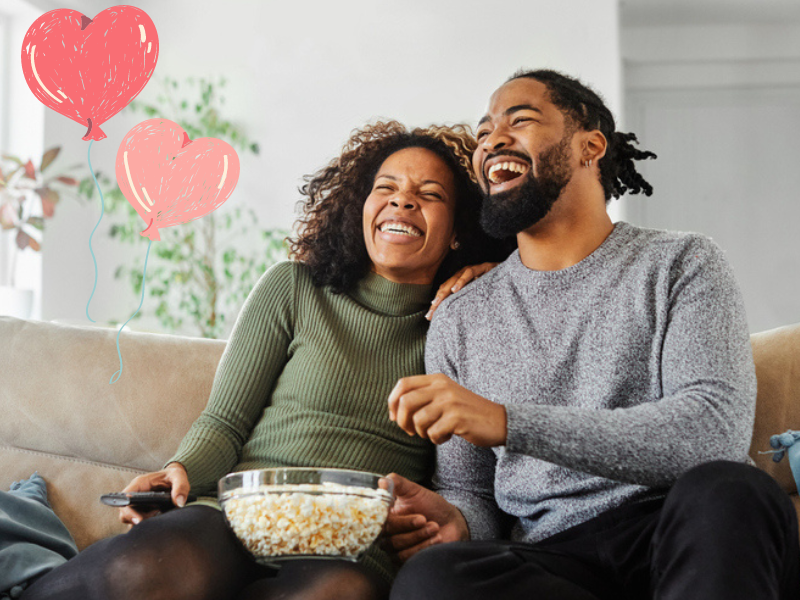 Couple watching a movie and laughing while eating popcorn