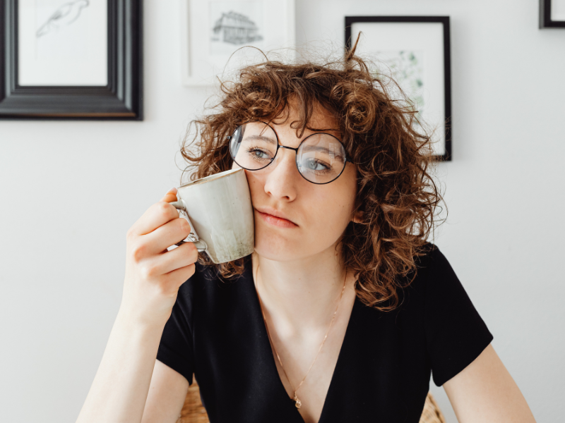 Curly haired woman holding a coffee mug and thinking