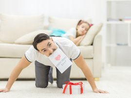 Dad holding gift while daughter sleeps on couch