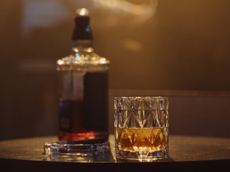Drinking glass with brown liquid beside bottle