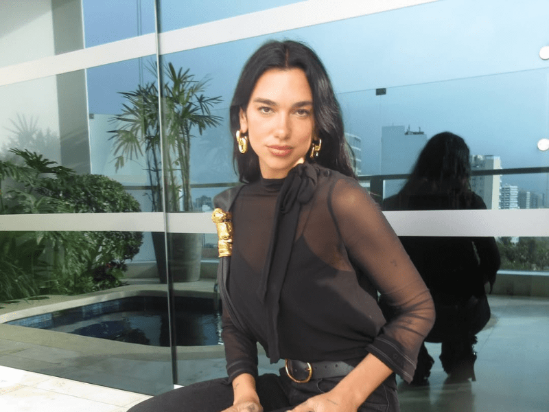 Dua Lipa poses on a balcony with a city skyline background
