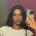 Dua Lipa takes a selfie next to a wall covered in graffiti