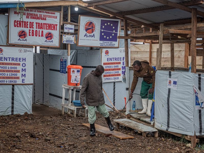 A hygiene worker disinfects a person's feet at the entrance to the Rwampara Ebola Treatment Centre