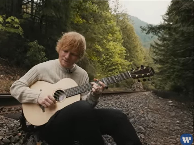 Ed Sheeran playing a guitar near a train track