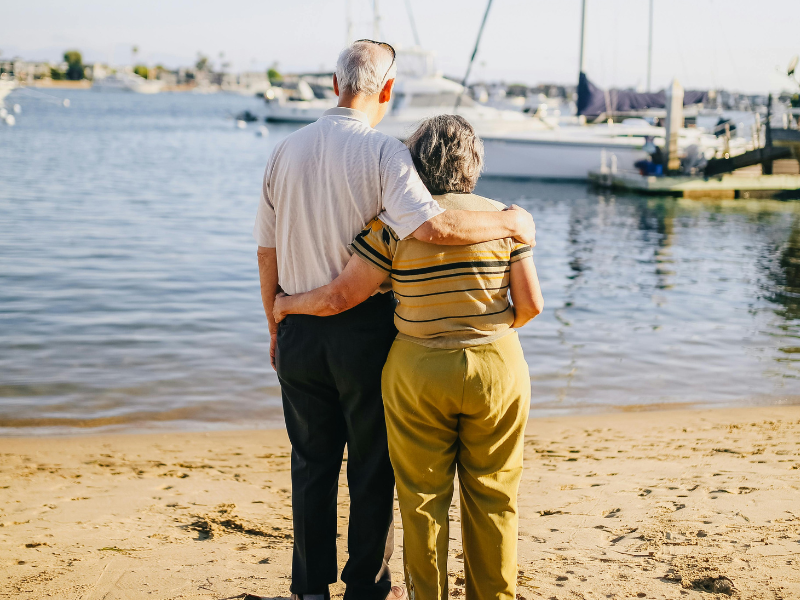 Elderly couple standing on the shore holding each other