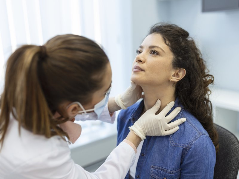 Endocrinologist examining throat of young woman in clinic